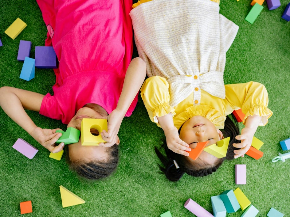 Before: Two children play with blocks on a rug in a cluttered room filled with scattered toys.